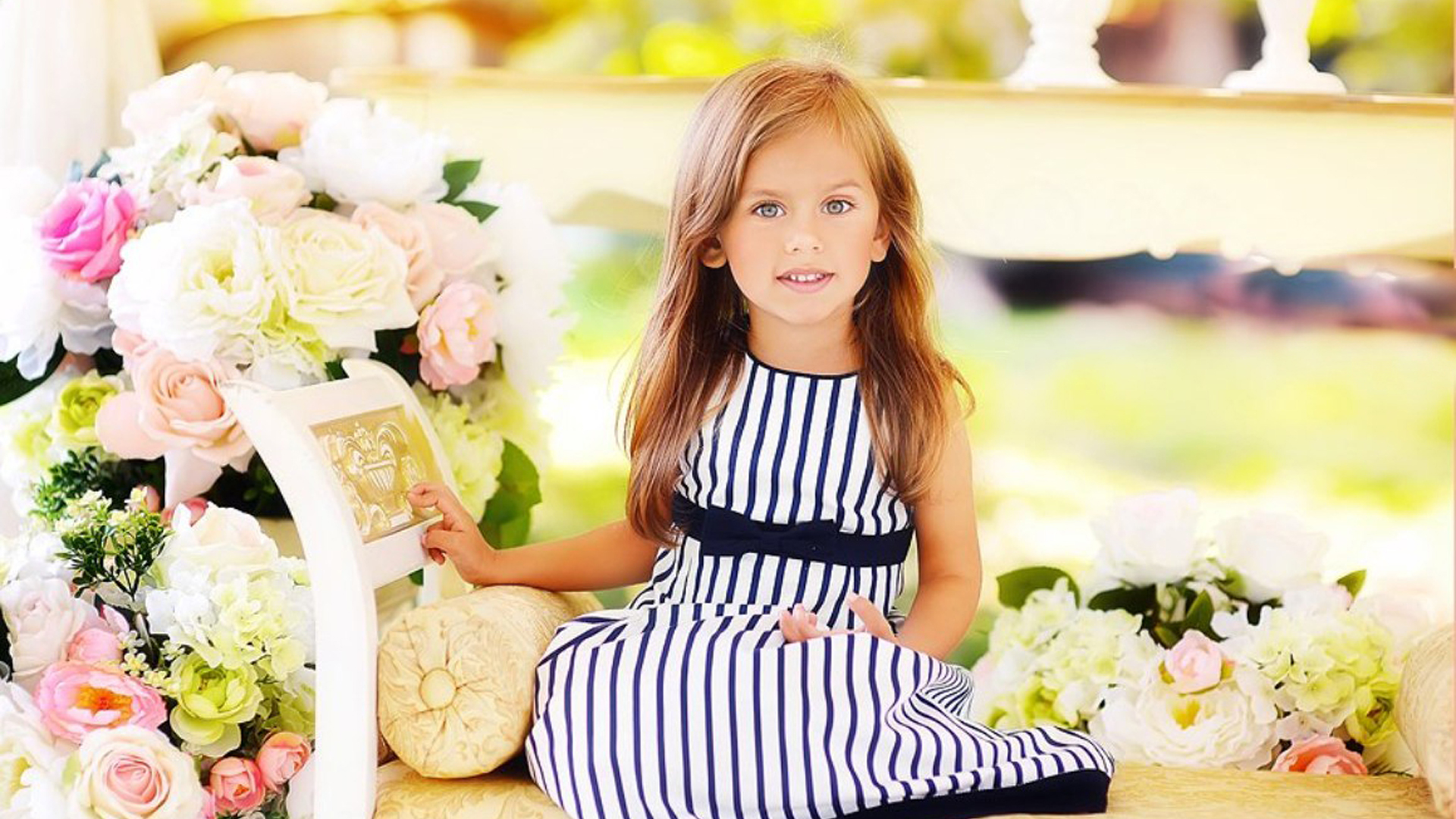 Cute Little Girl Is Sitting On Couch Wearing Blue White Lines Design Dress In Colorful Blur Wallpaper 2K Cute