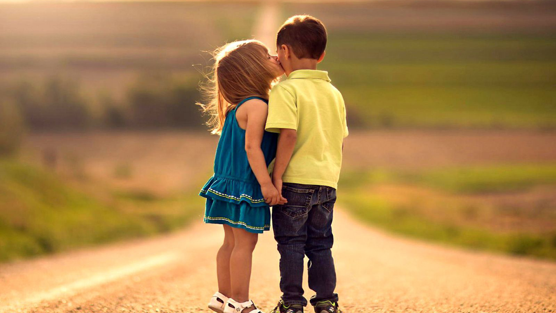 Little Girl Is Kissing Boy Wearing Blue Yellow Dress In Green Blur Wallpaper 2K Couple