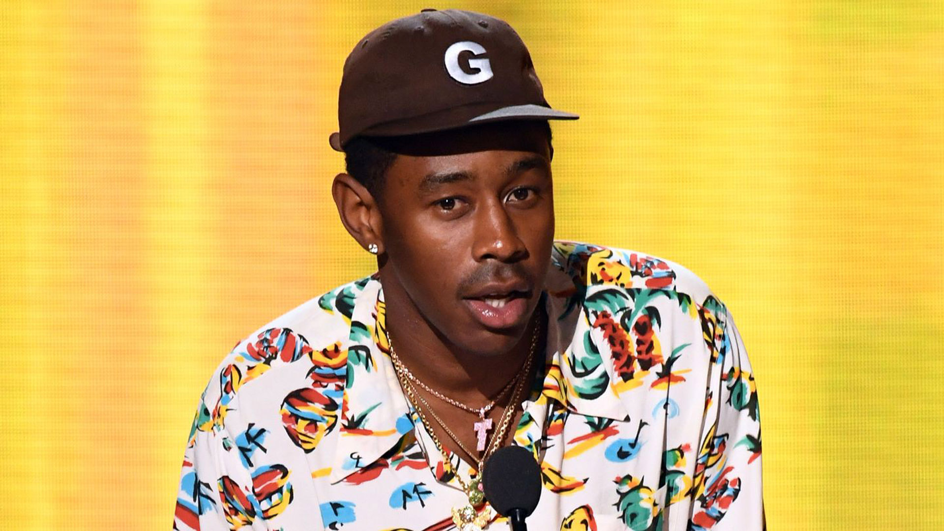 Tyler The Creator Is Wearing Colorful Shirt And Brown Cap Standing In Yellow Wallpaper 2K Tyler The Creator