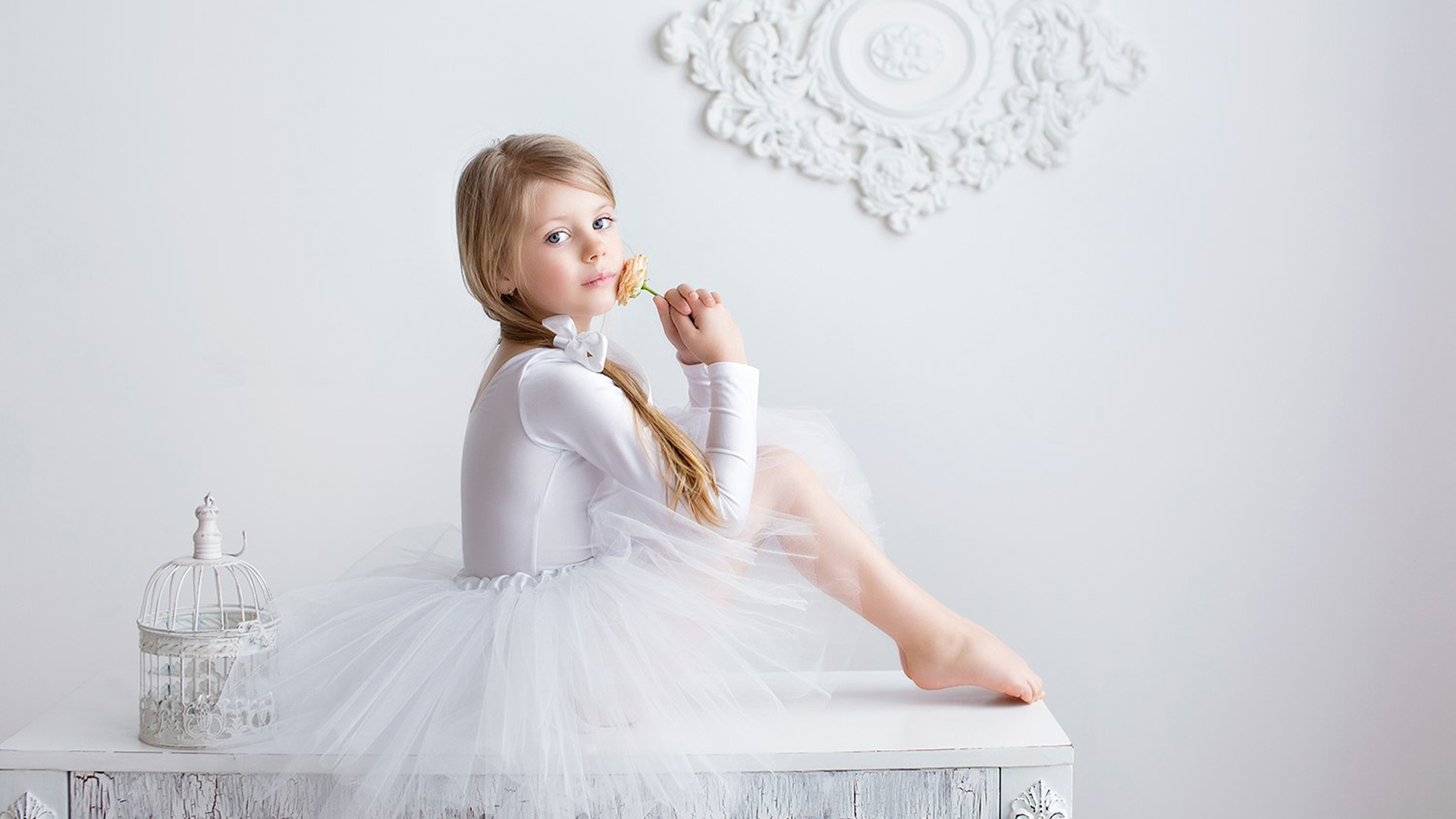 Cute Little Girl Is Sitting On White Table Wearing White Dress In White Wall Wallpaper 2K Cute