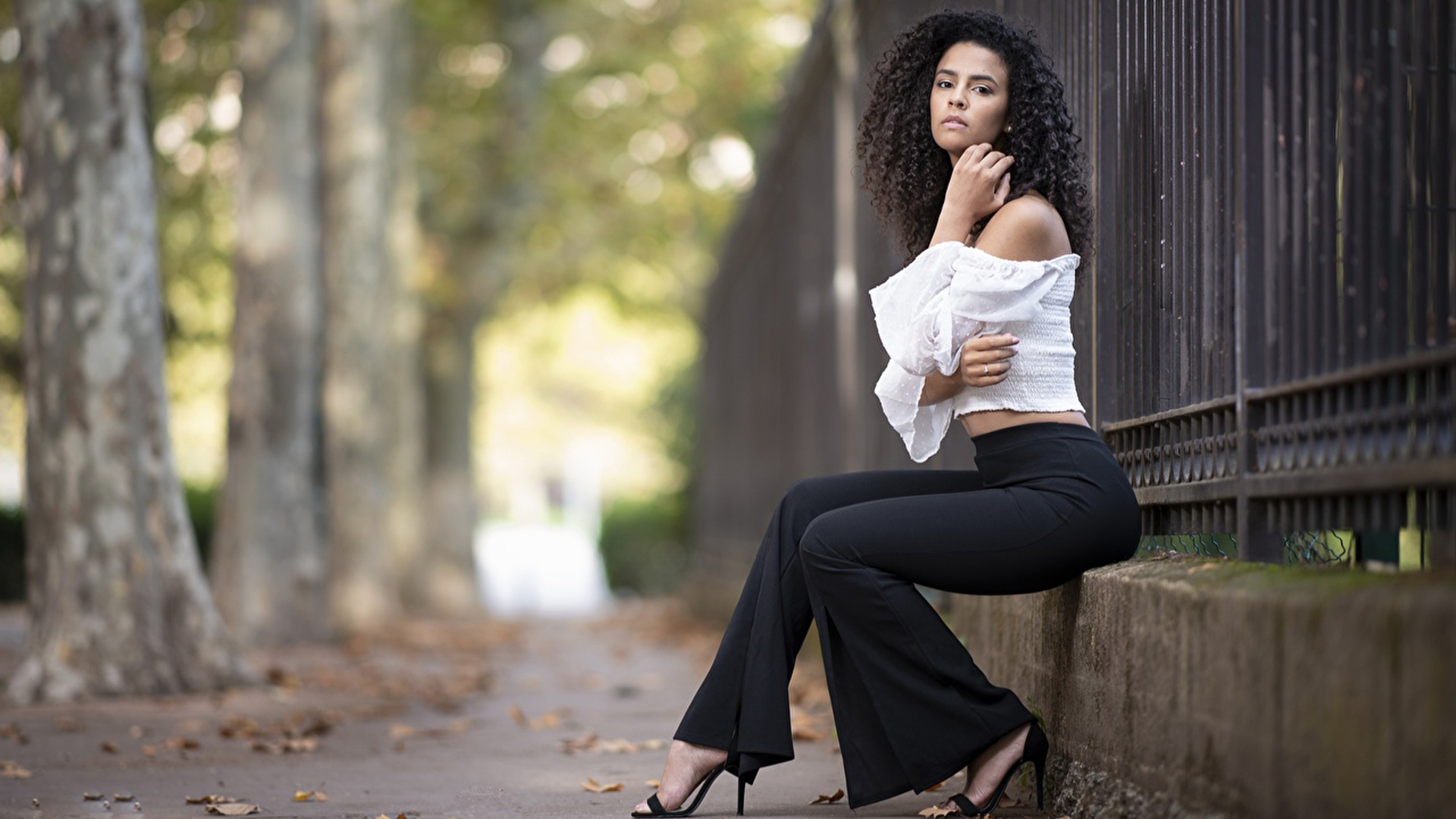 Curly Hair Girl Model Is Wearing White 4K And Black Pants Sitting In Fence Wallpaper 2K Girls