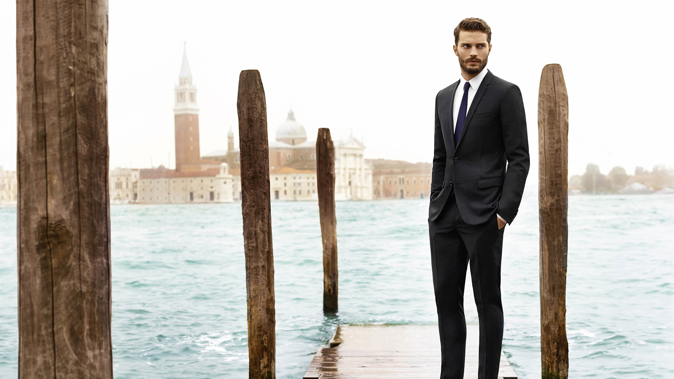 Jamie Dornan Is Standing On Wooden Dock Wearing Black Coat Suit In River Wallpaper 2K Boys
