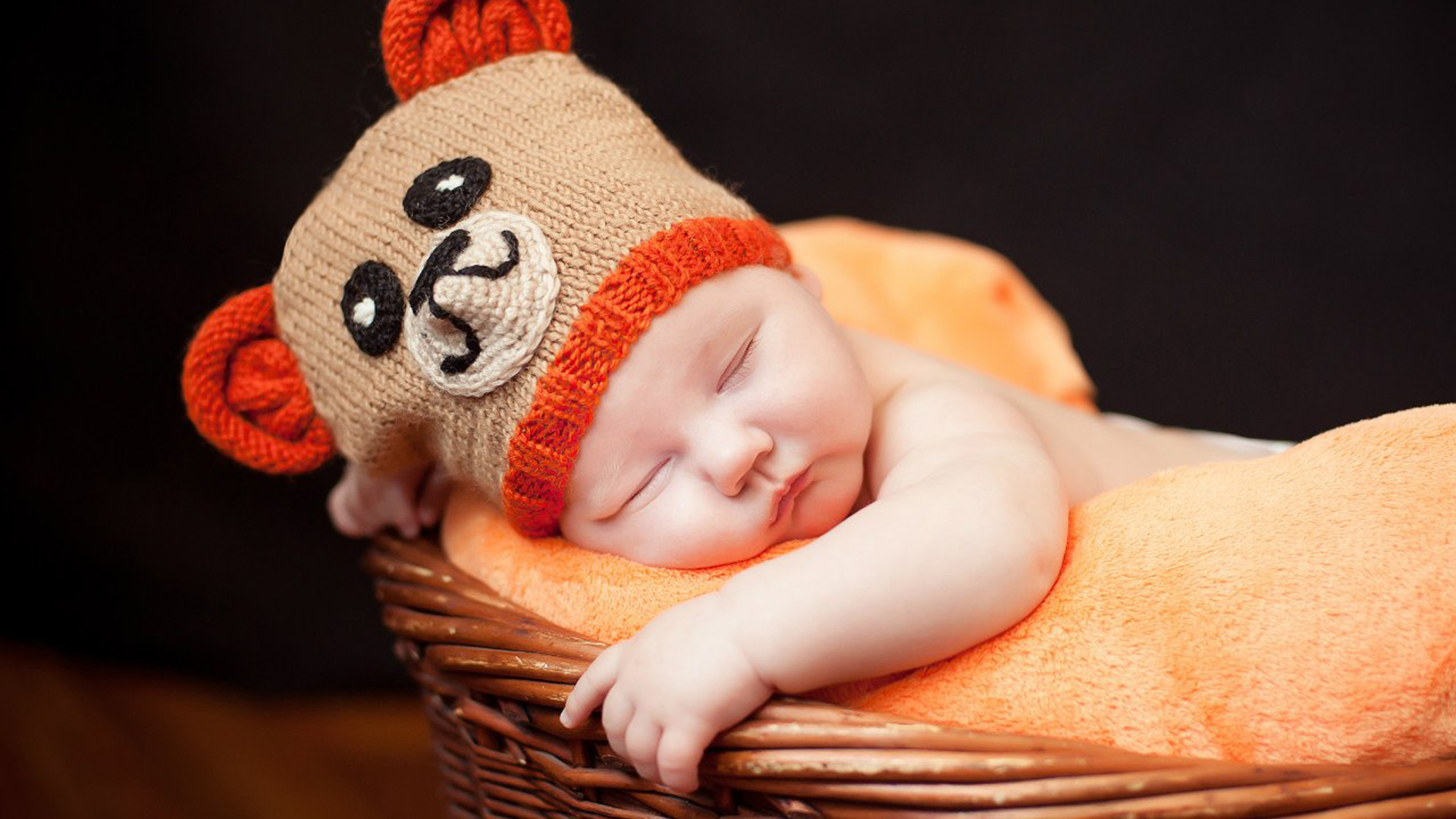 Cute Baby Toddler Is Sleeping Inside Wood Basket On Soft Light Orange Towel Wearing Woolen Knitted Cap In Dark Wallpaper 2K Cute