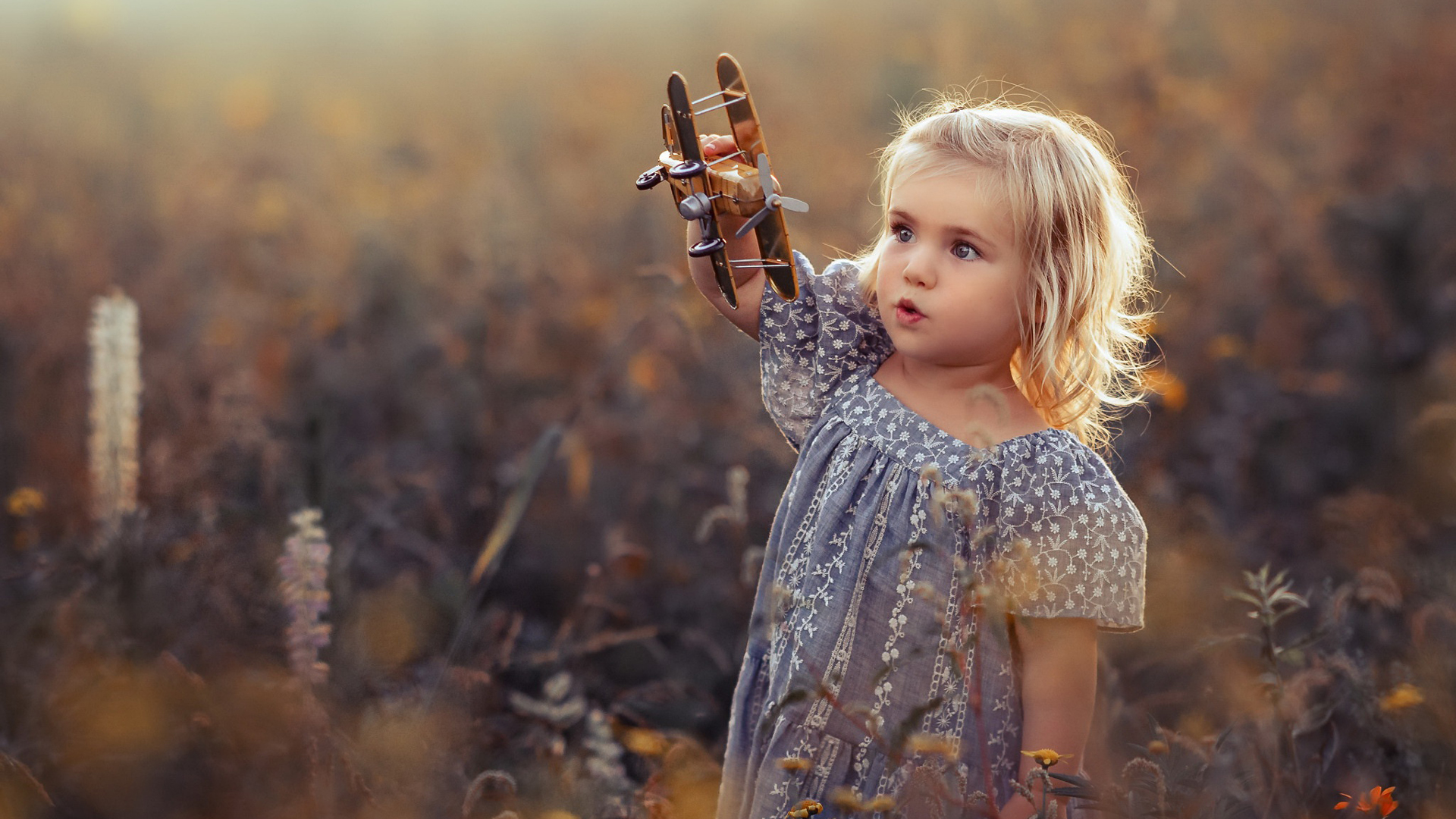 Cute Little Girl Is Standing In The Middle Of Flowers Field Wearing Printed Frock Playing With Toy 2K Cute