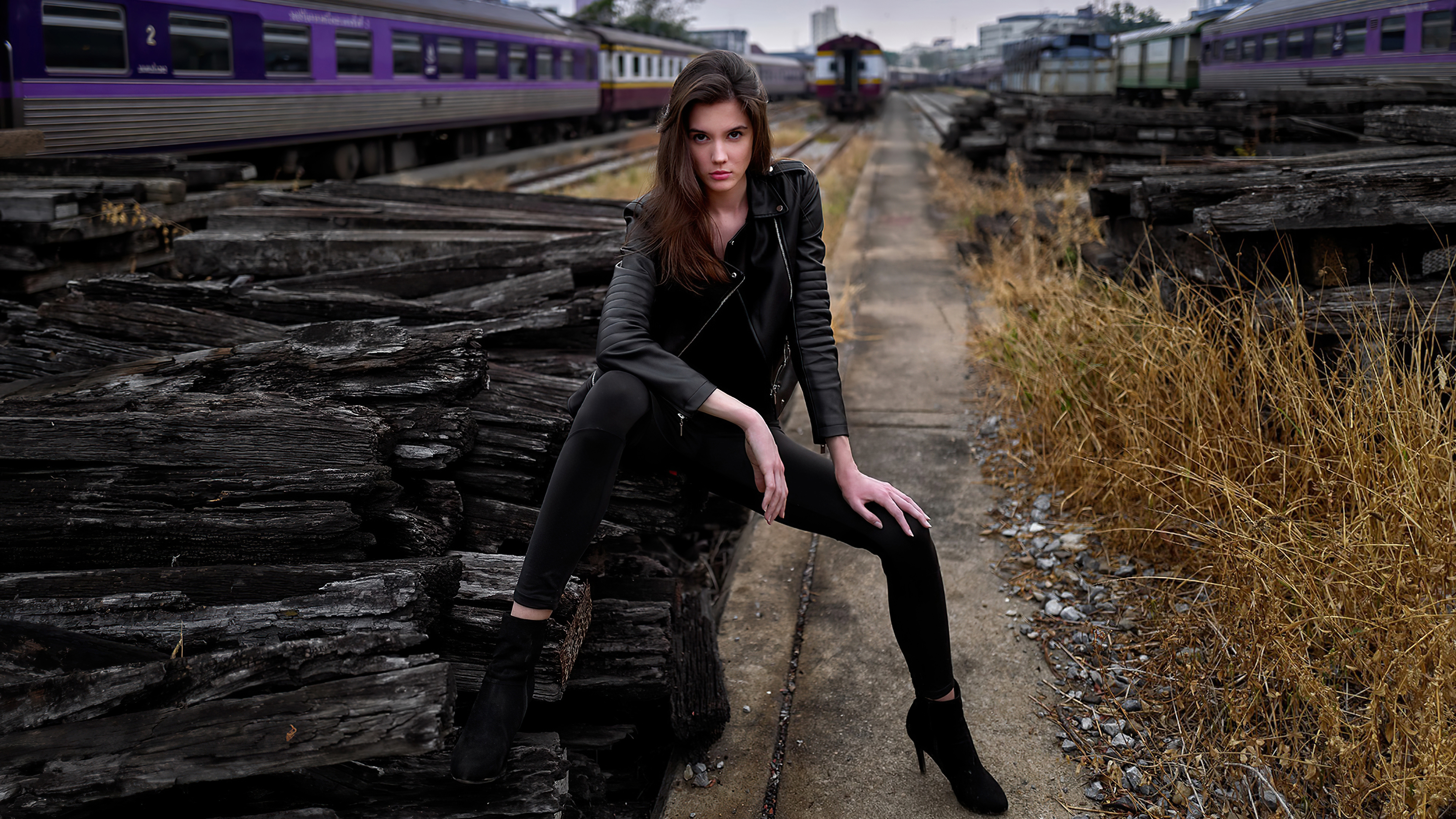 Brunette Girl Model Is Sitting On Wood Log Wearing Black Leather Jacket In Blur Train Wallpaper K 2K Girls