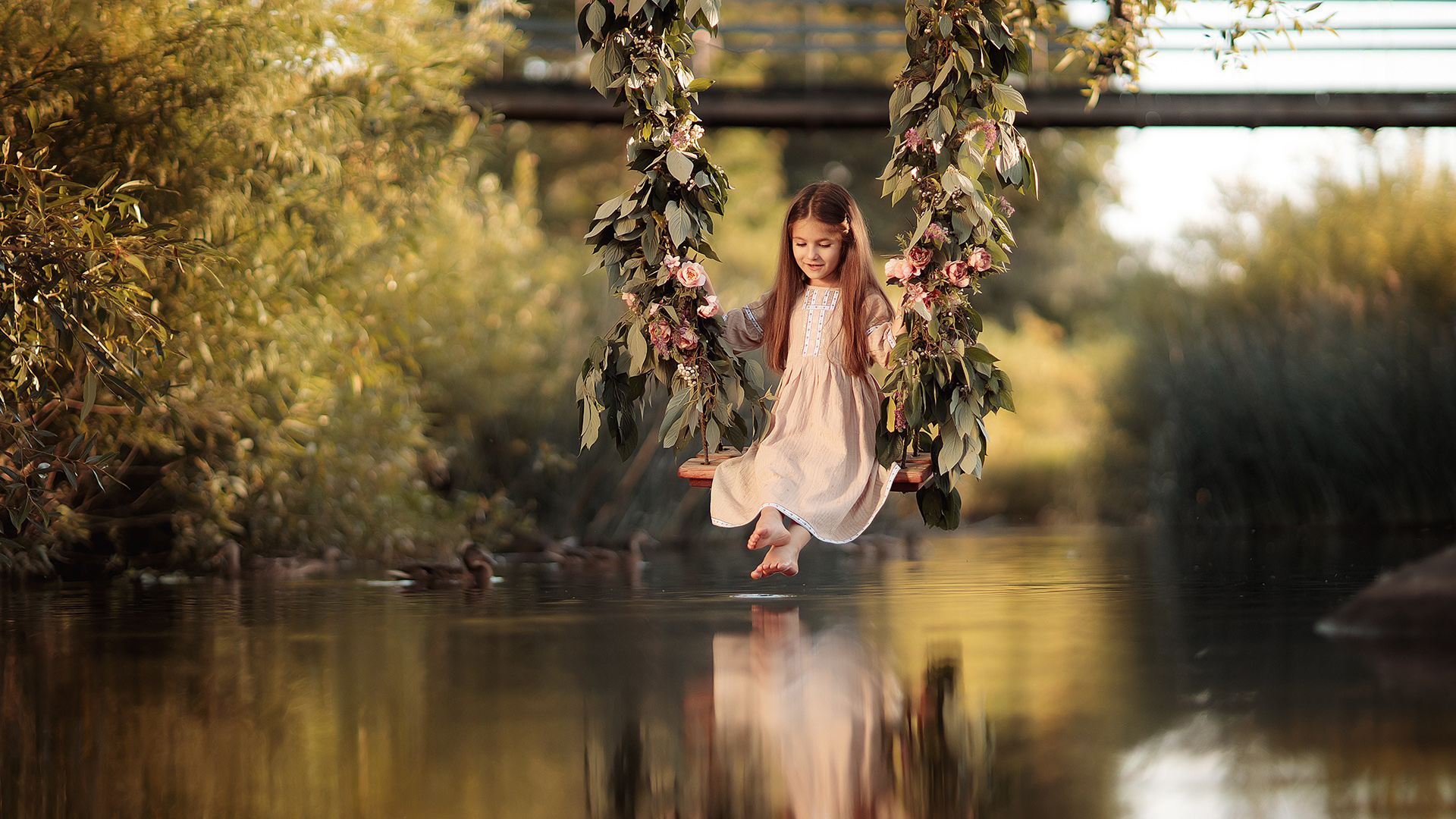 Cute Little Girl Is Sitting On Flower Swing Above Body Of Water With Reflection 2K Cute